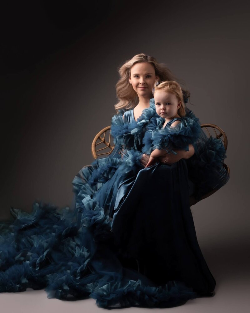 Mother and daughter sitting wearing matching gown in petrol blue by rosa amour