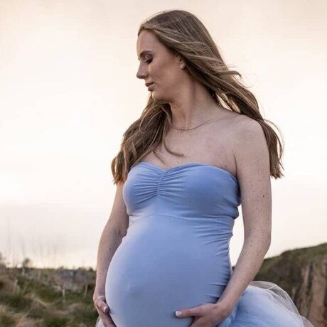 Pregnant women standing holding bump outdoors