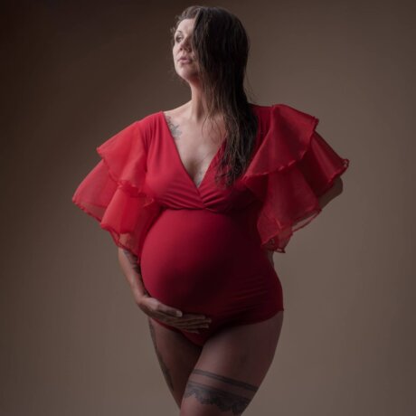 Pregnant women posed in red maternity bodysuit holding bump