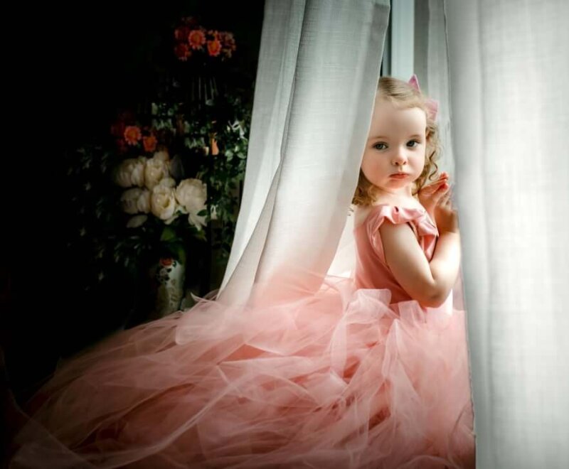 little girl posing in window under curtains wearing rosa amour children's gown