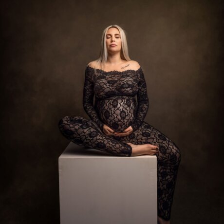 Pregnant women posed on cube in a black floral lace jumpsuit by rosa amour