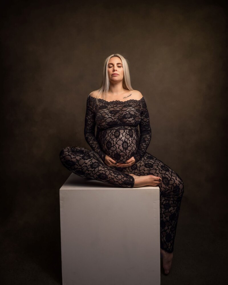 Pregnant women posed on cube in a black floral lace jumpsuit by rosa amour