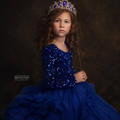 Little girl posing wearing a tiara in a sequin royal blue dress