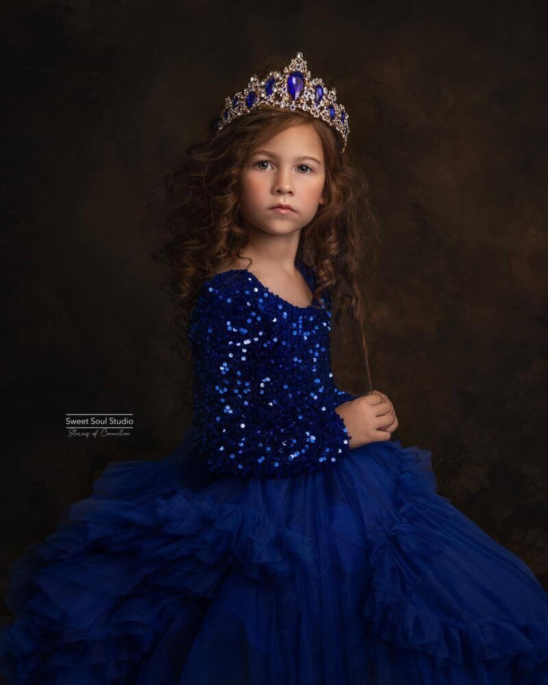 Little girl posing wearing a tiara in a sequin royal blue dress